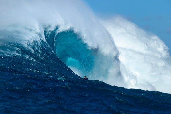 Surfer riding a large wave in the ocean with a clear sky.