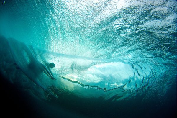 Underwater view of a surfer riding a wave with sunlight filtering through the water.