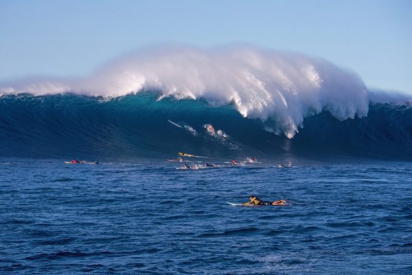 Surfers waiting for waves in the ocean with a large wave in the background