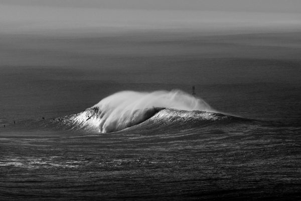 Black and white photo of a surfer riding a large wave in the ocean.
