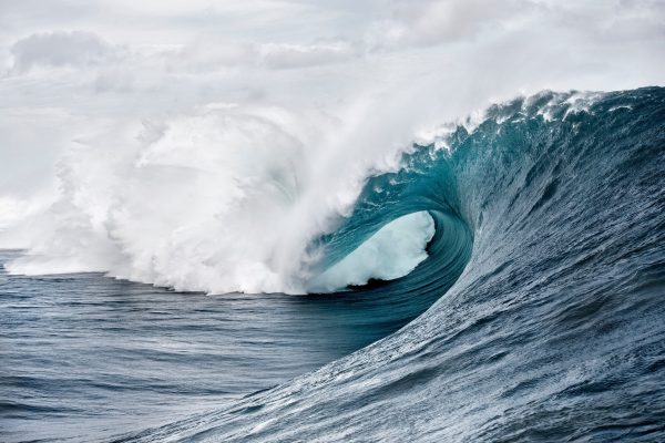 Large ocean wave with white foam curling over itself against a cloudy sky.