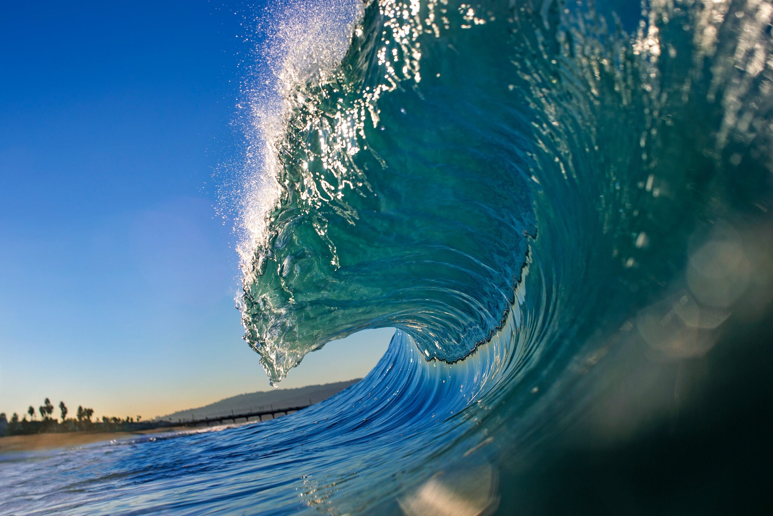 Close-up of a breaking big wave with clear blue sky and beach in the background