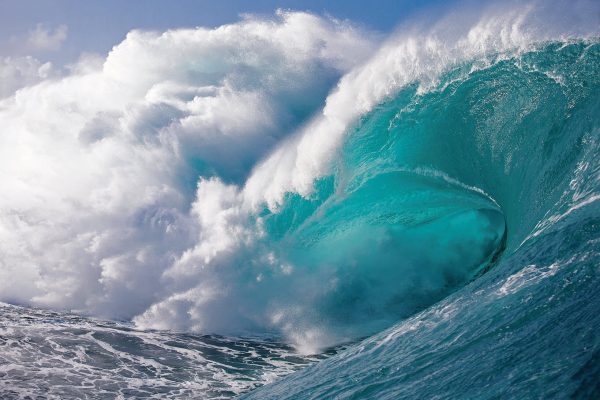 A big large ocean wave with white foam against a blue sky curling, its ineffable.
